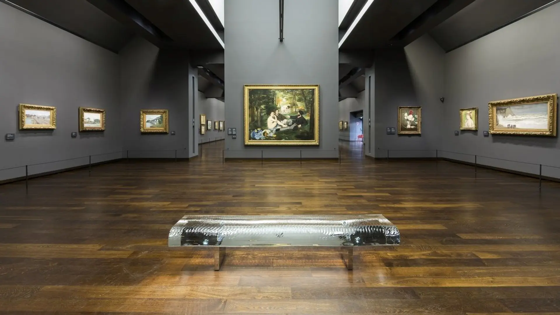 Large room with wooden floor, one chair and grey walls filled with painting at Musee D'Orsay